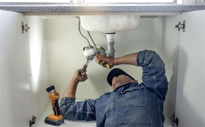 Plumber repairing pipes beneath a bathroom sink in Zephyrhills