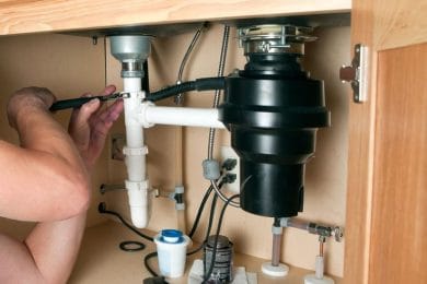 Plumber repairing a garbage disposal beneath a kitchen sink in Zephyrhills