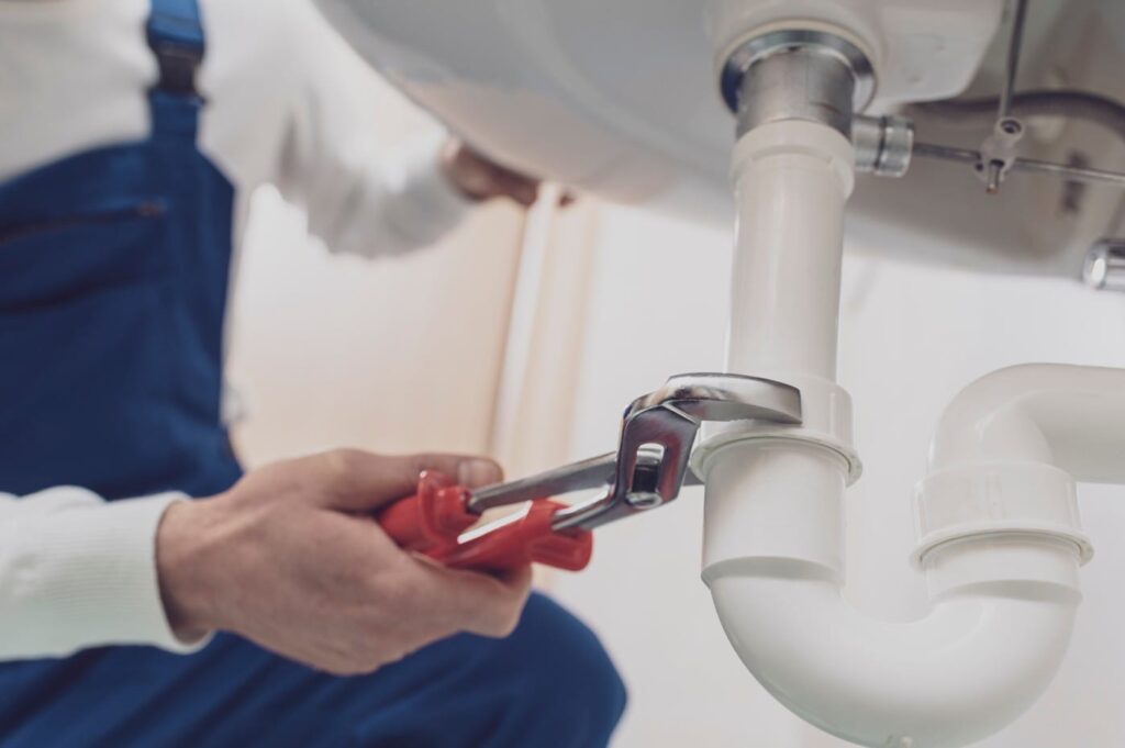 Plumber repairing a white drain pipe beneath a sink in Zephyrhills